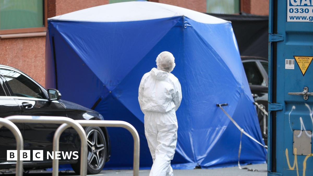 A blue forensic tent is erected in the street with an officer dressed in white overalls walking towards to. A black car is parked next to the tent
