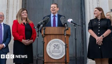 Rhun ap Iorwerth stands at a lectern surrounded by members of his cabiney