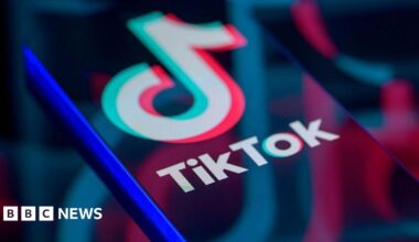 TikTok logo displayed on a smartphone screen, with enlarged, faded versions of the logo reflected across it.