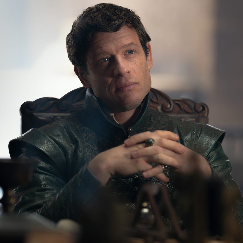 a seated person in dramatic attire hands clasped background suggests a formal setting a seated person in dramatic attire hands clasped background suggests a formal setting