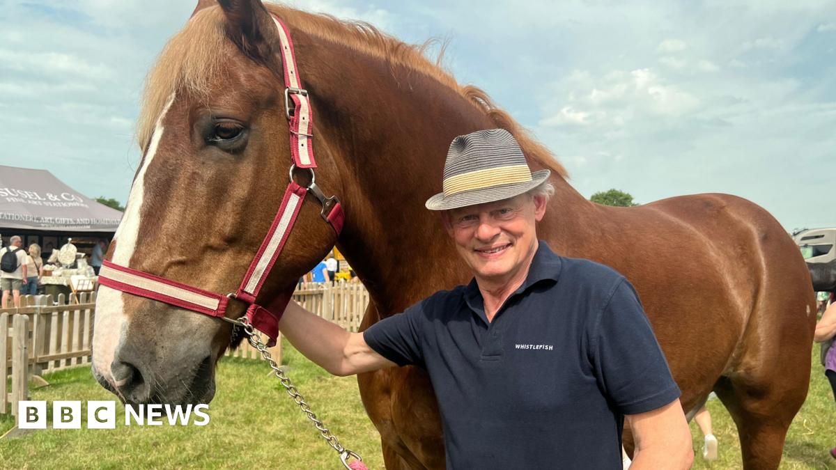 Martin Clunes is standing next to a horse wearing a hat and T-shirt.