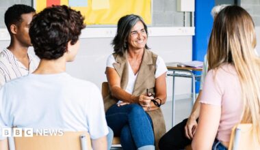 A smiling lady leads a discussion with four other people sitting in a circle