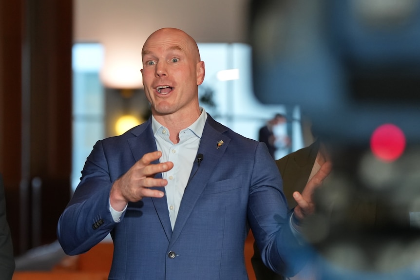 A politician in a blue shirt and blazer speaks animatedly.