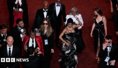 Actor and singer Teyana Taylor wearing a fitted gown of black and white feathers as she shimmies down the red carpet of the Acadamy Awards surrounded by other attendees.