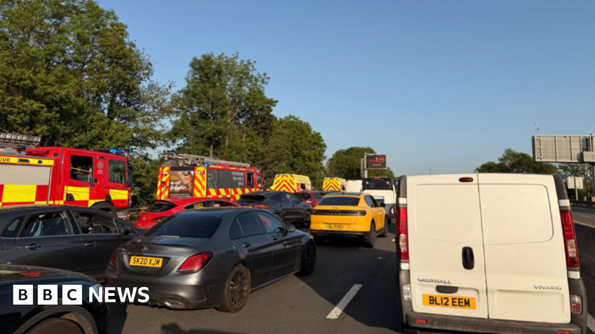 A queue of cars and vans on a motorway with a number of fire engines on the left hand side