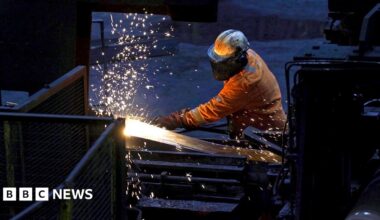 A steelworker wearing orange protective gear welds as sparks flies against a dark background in Scunthorpe Steel works in 2025.