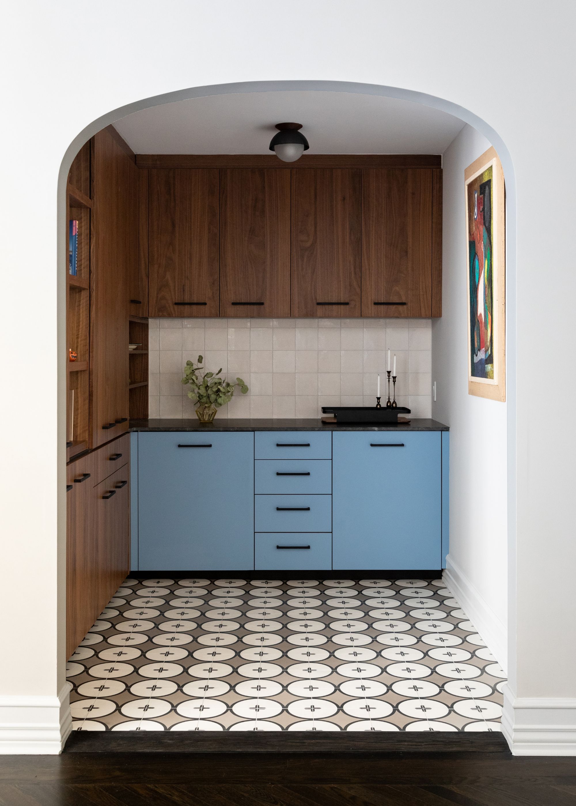 A small modern kitchen with bright blue lower cabinets, white wall tiles, wooden upper cabinets and gray, black, and cream floor tiles.