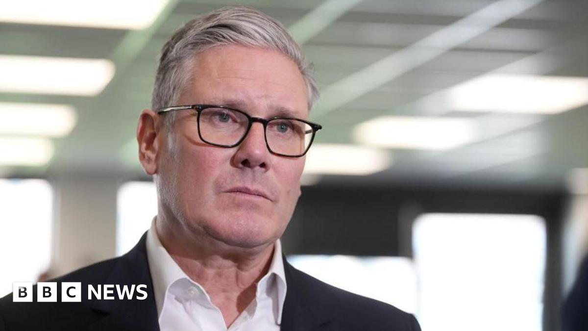 Sir Keir Starmer, who has grey short hair styled in a side parting and wears thin-rimmed glasses, a white shirt and black suit jacket, looks serious
