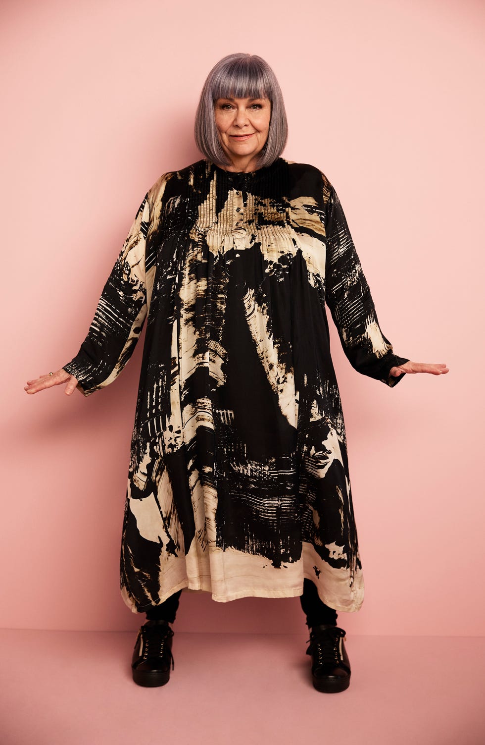 a person wearing a black and beige patterned oversized dress against a pink background a person wearing a black and beige patterned oversized dress against a pink background