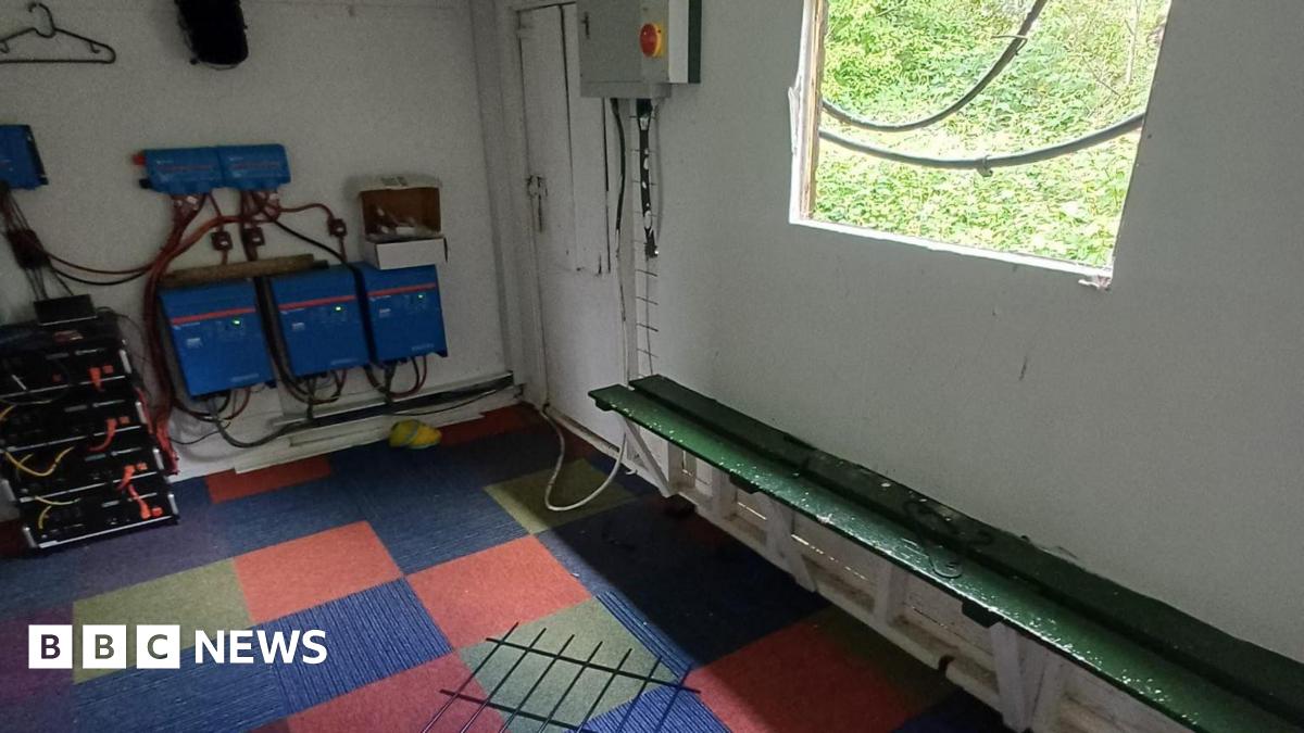 A room with a broken window and a wooden board, which has fallen on a chequered carpet.