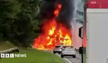 Firefighters on a section of closed dual carriageway. A fire engine and badly-burned lorry are to the left