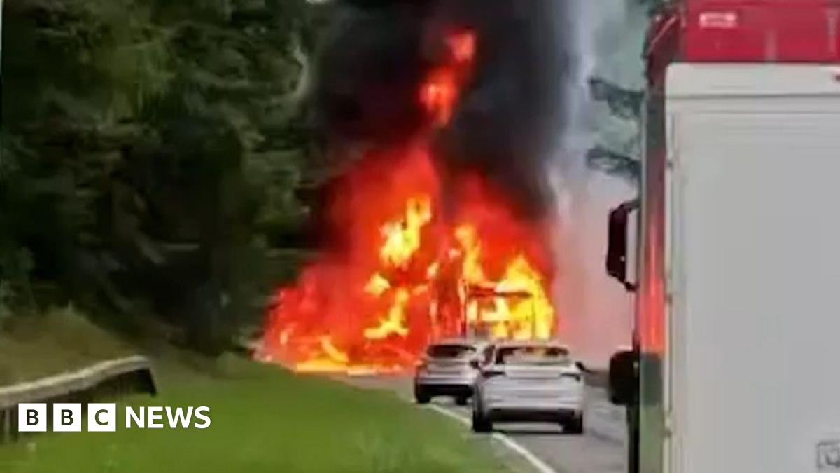 Firefighters on a section of closed dual carriageway. A fire engine and badly-burned lorry are to the left