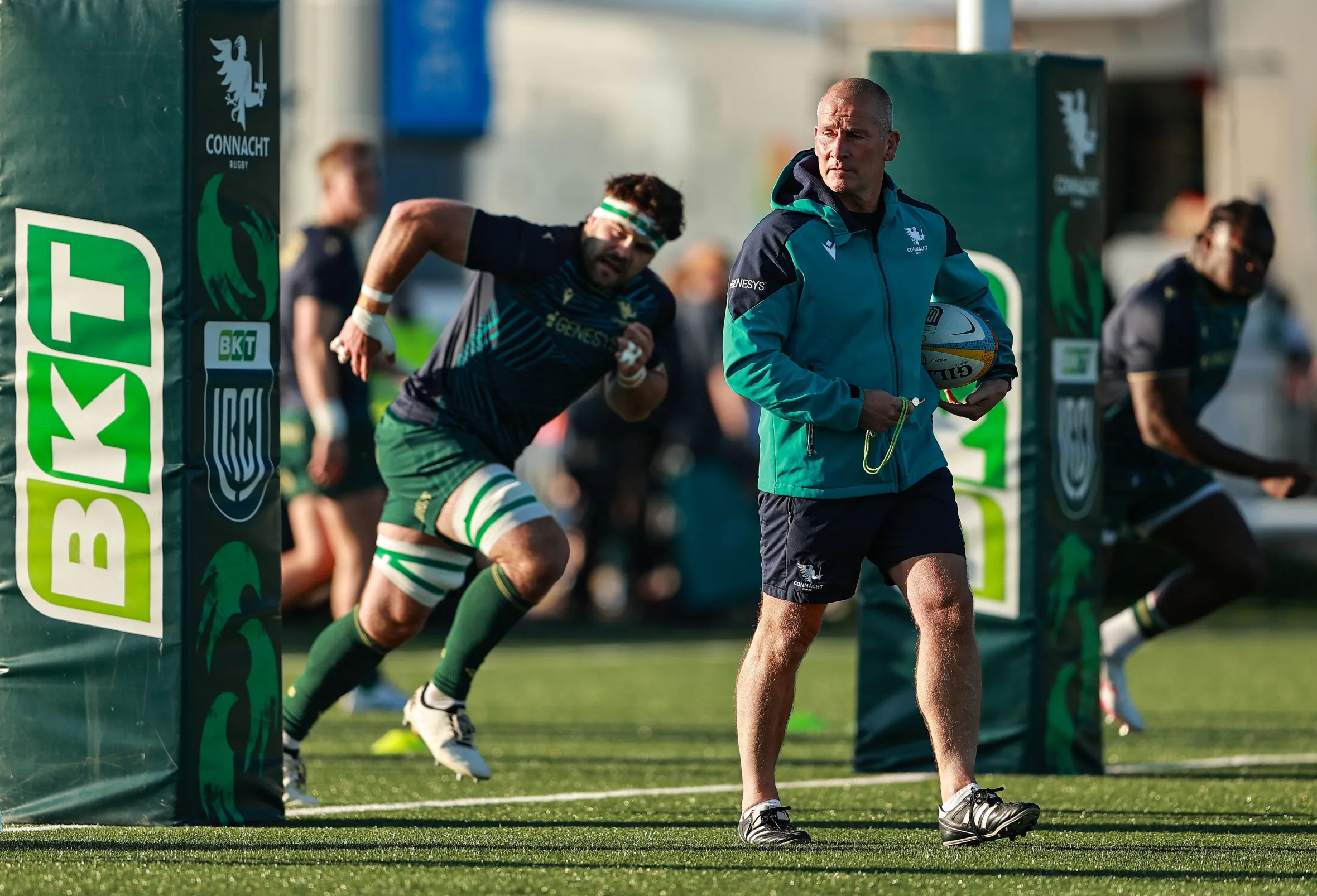 Connacht head coach Stuart Lancaster holds a rugby ball on the field.