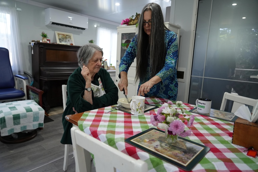 A woman cuts food up for an elderly woman.