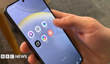 A hand holding a black mobile phone with six apps on the screen: Meta AI, ChatGPT, Gemini, Grok, Copilot, Claude.