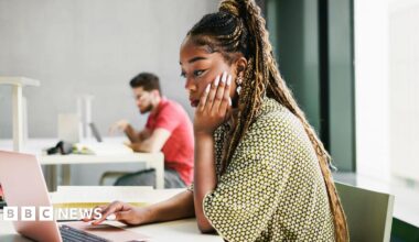 A young woman working from a laptop in an modern office.
