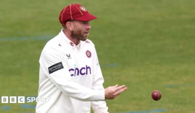 Luke Procter throws a red cricket ball to an unpictured player
