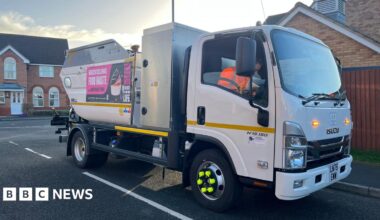 A small white bin lorry on a road in a residential area.