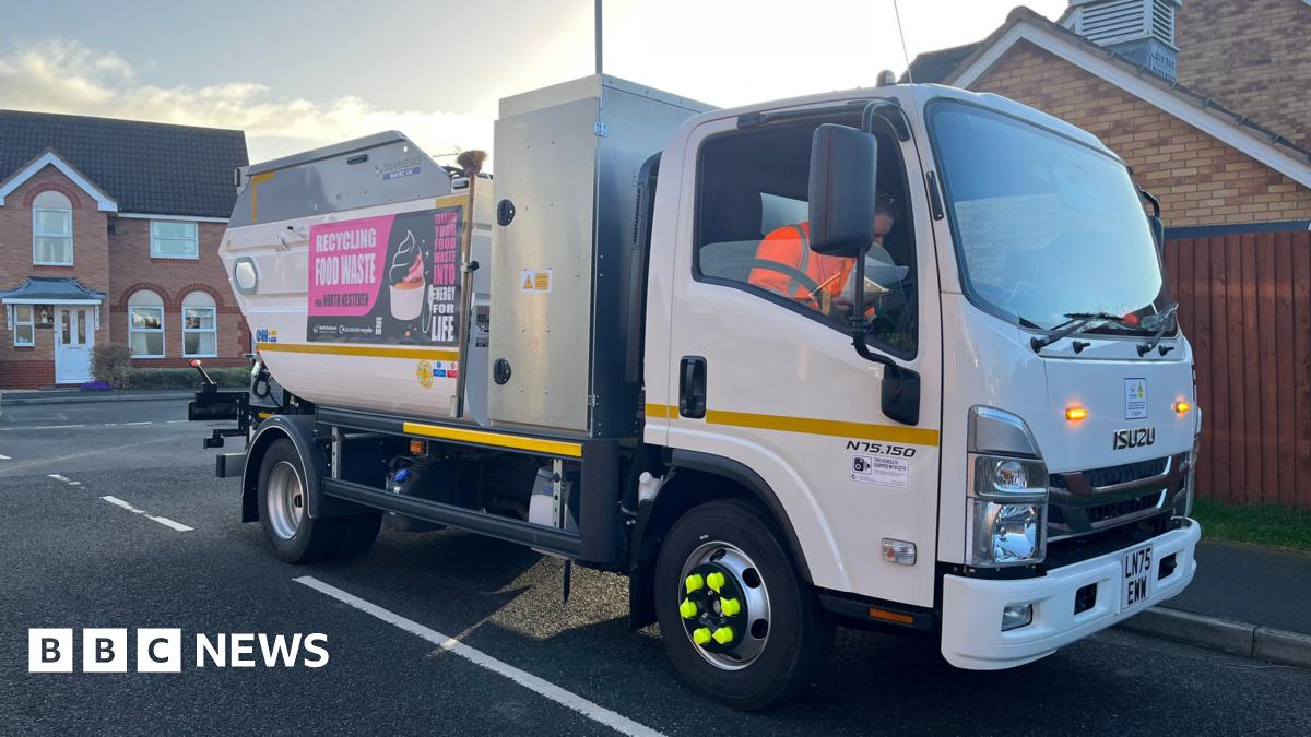 A small white bin lorry on a road in a residential area.