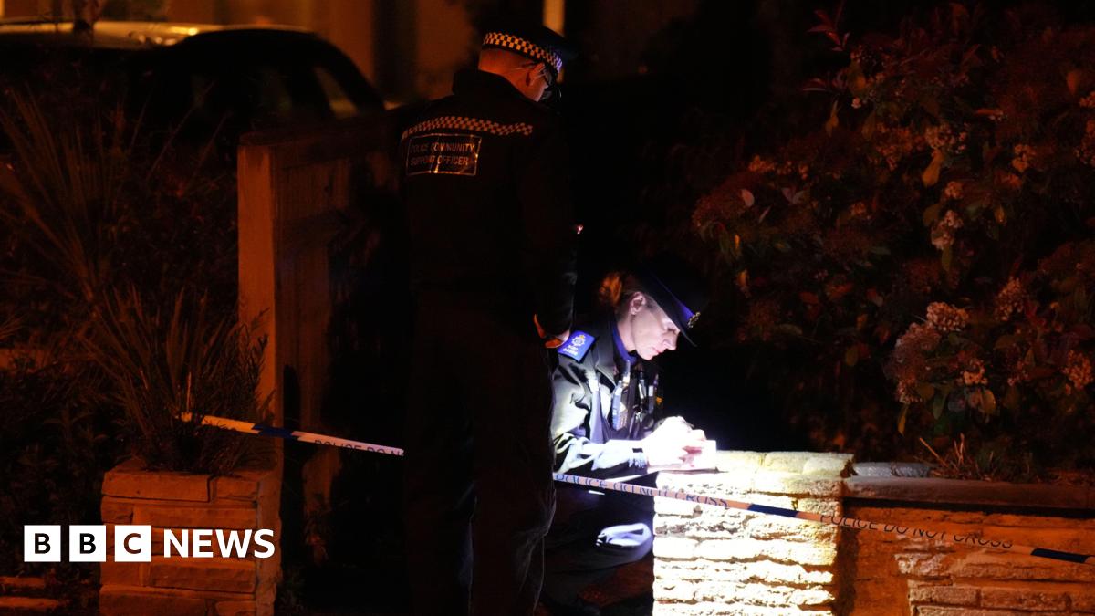 Two police officers outside at night. One is crouching down and writing on a notepad while her colleague shines a light on her.