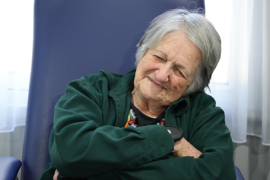 An elderly woman smiles as she sits in her chair at home.