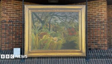 Surprised! by Henri Rousseau reproduction in a gold frame mounted on a briack wall