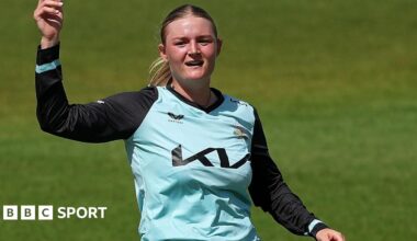 Ryana MacDonald-Gay in a light blue shirt points to the sky before bowling