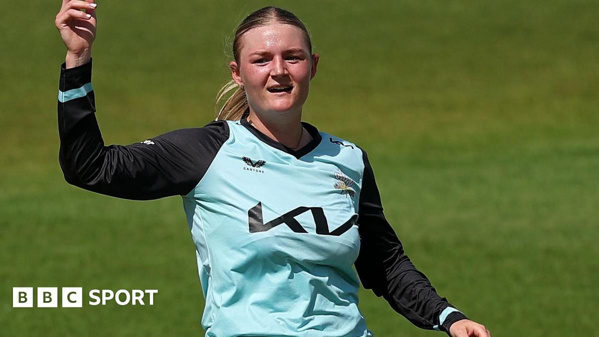 Ryana MacDonald-Gay in a light blue shirt points to the sky before bowling