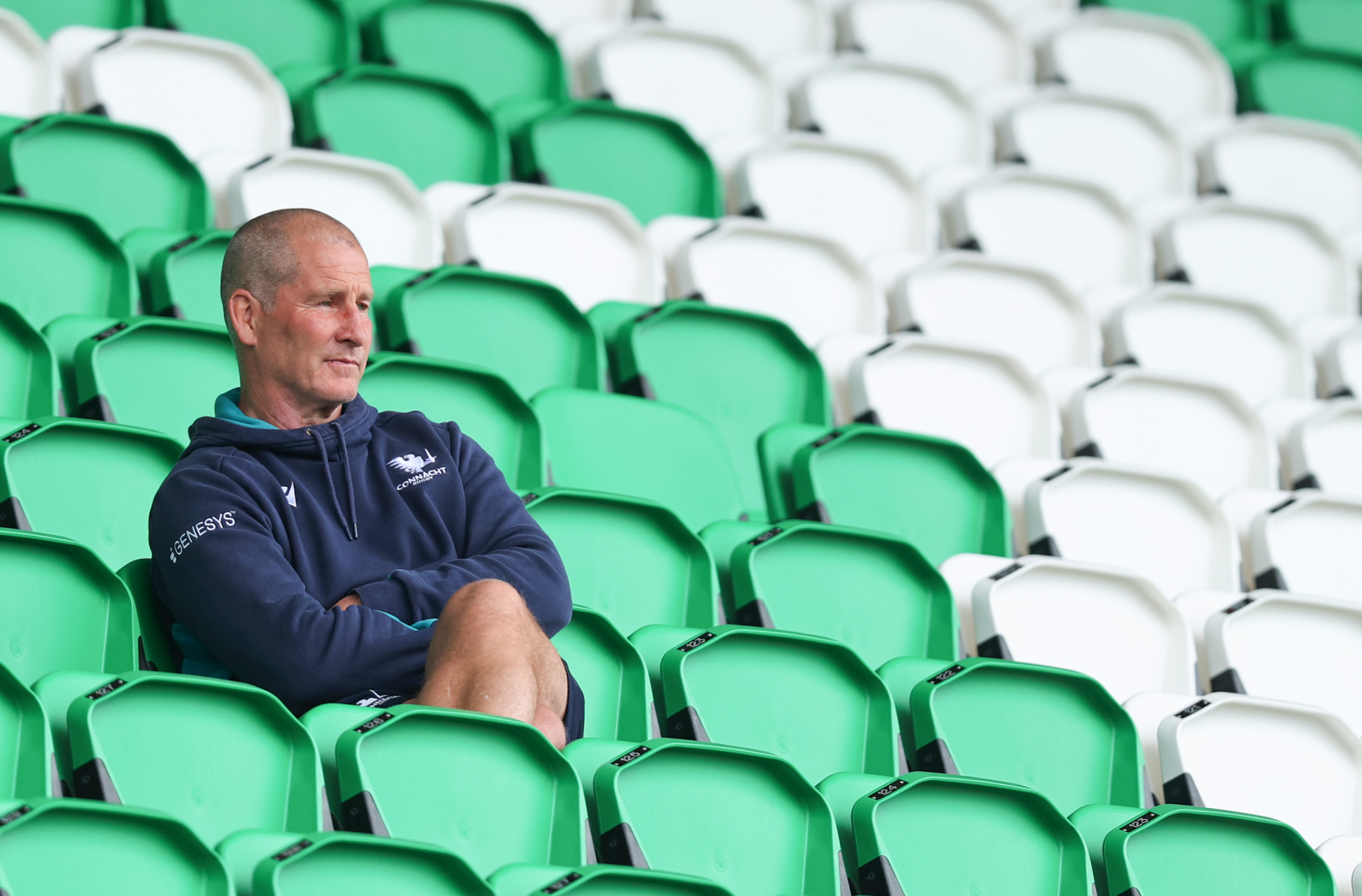 Connacht head coach Stuart Lancaster sits in a green stadium seat, wearing a navy hoodie.