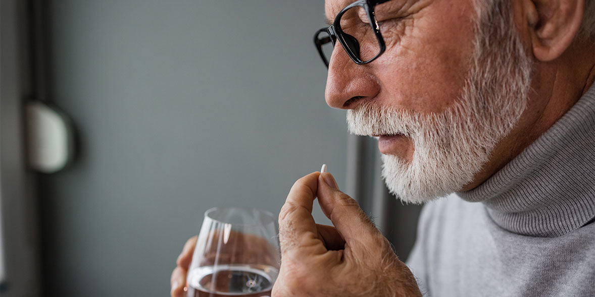 An older man who is just about to put a supplement in his mouth.