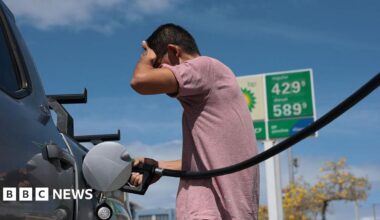 A man palms his forehead in frustration while filling his truck up with gasoline.
