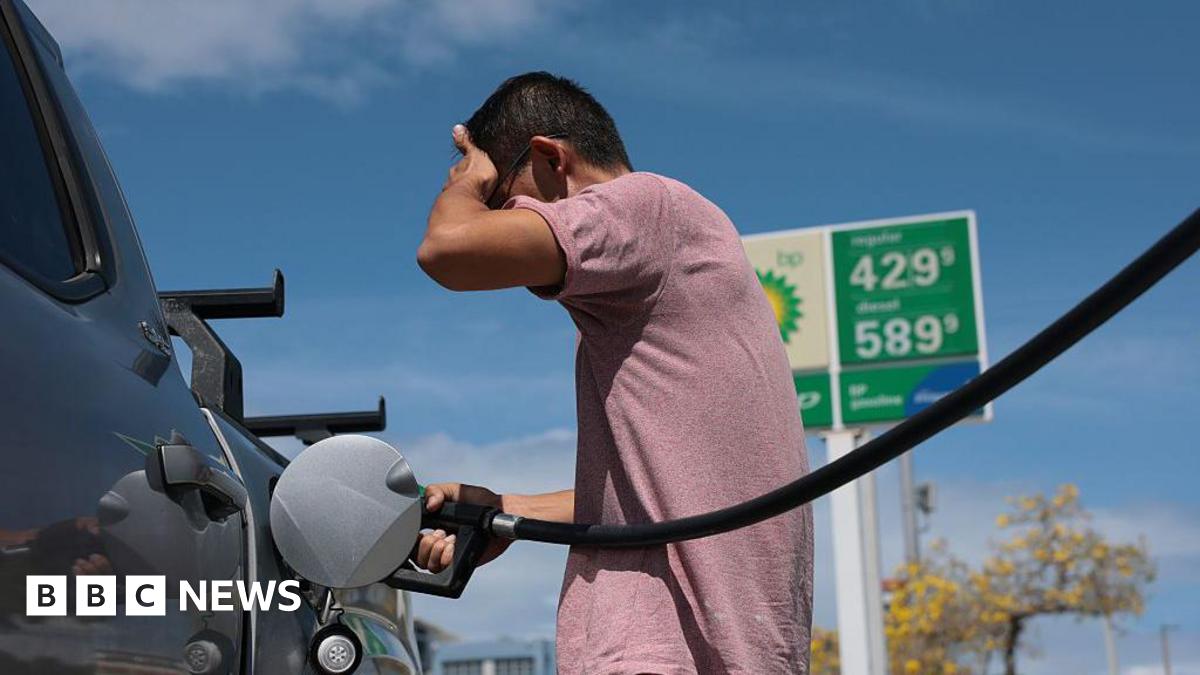 A man palms his forehead in frustration while filling his truck up with gasoline.