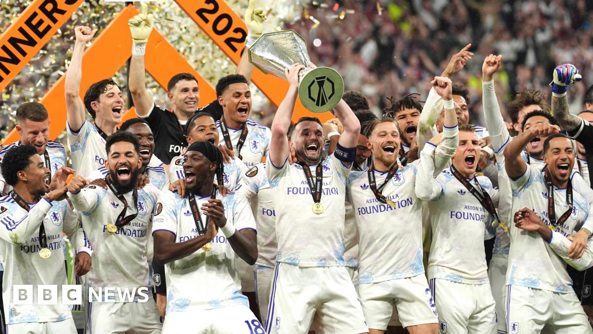 The Aston Villa team, made up of about 20 men, all wearing white uniforms with blue accents, are grouped together cheering. In the centre one of them is holding a large trophy above his head