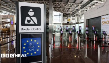 A border control sign showing a styalised image of a border control officer above a square version of the blue EU flag with yellow stars sits in an airport area in front of new machines for checking biometrics.