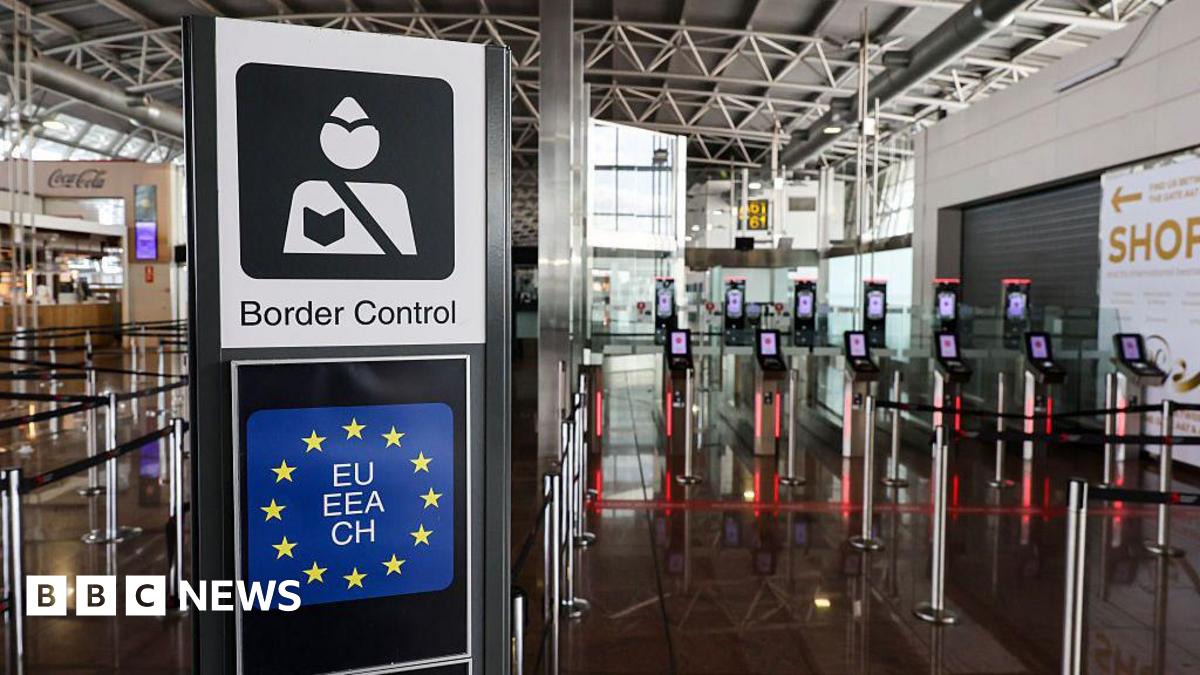 A border control sign showing a styalised image of a border control officer above a square version of the blue EU flag with yellow stars sits in an airport area in front of new machines for checking biometrics.