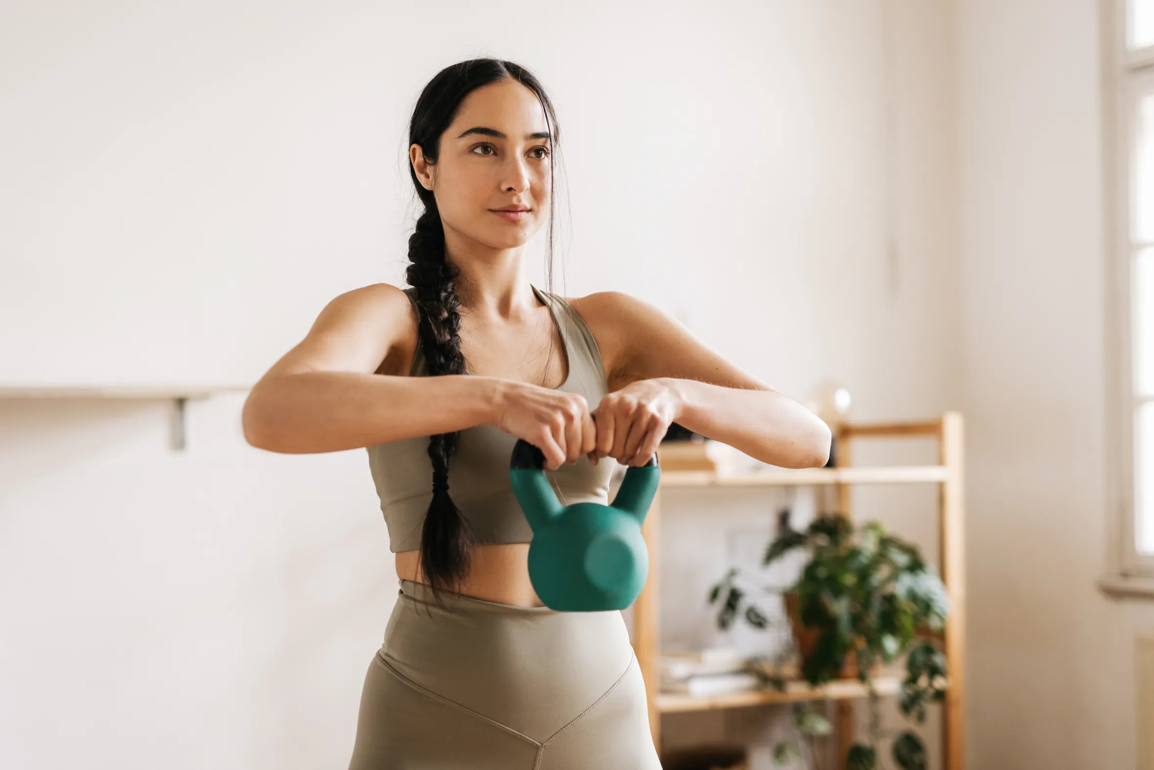 A sporty woman with a braid exercising with a green kettlebell.