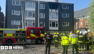 Firefighters at a block of flats, with a ladder against the building.