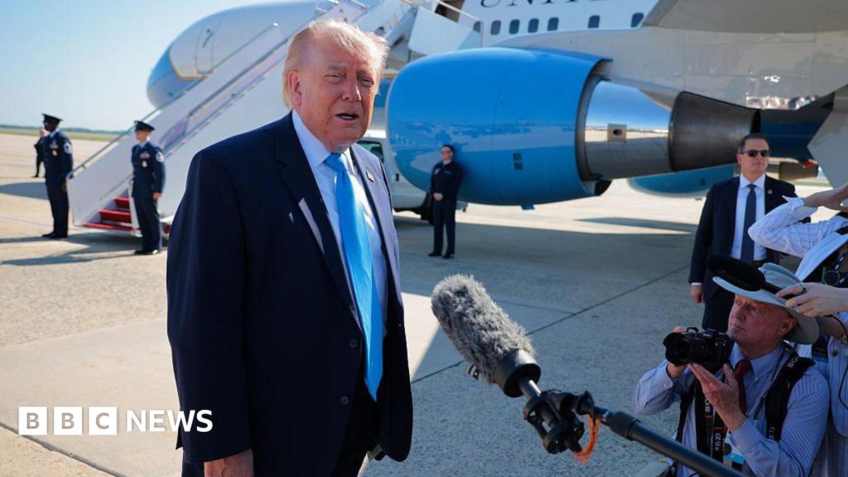 Trump wearing a suit and speaking to reporters, with a plane parked behind him.