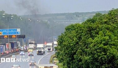 Cars and lorries travelling on the motorway with a fire visible in the background