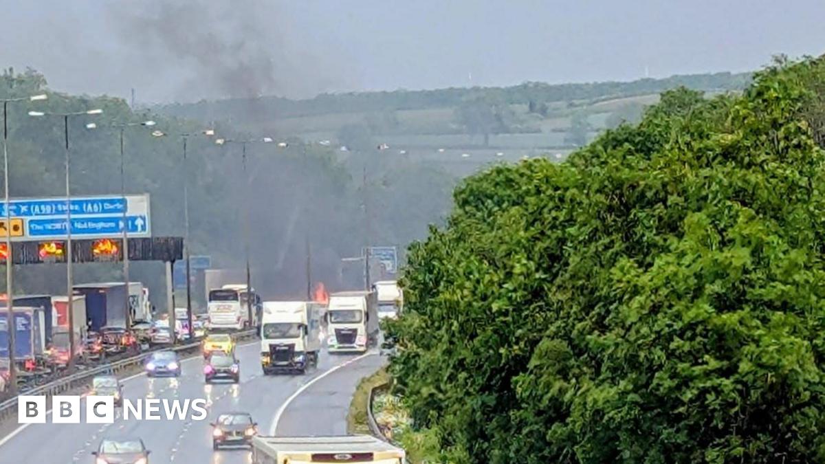 Cars and lorries travelling on the motorway with a fire visible in the background
