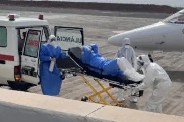 Medical workers in hazmat suits transferring a patient on a stretcher from an ambulance to a plane.