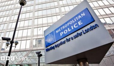 The well-known triangular Metropolitan Police sign is in the foreground of the image with the police headquarters in the background