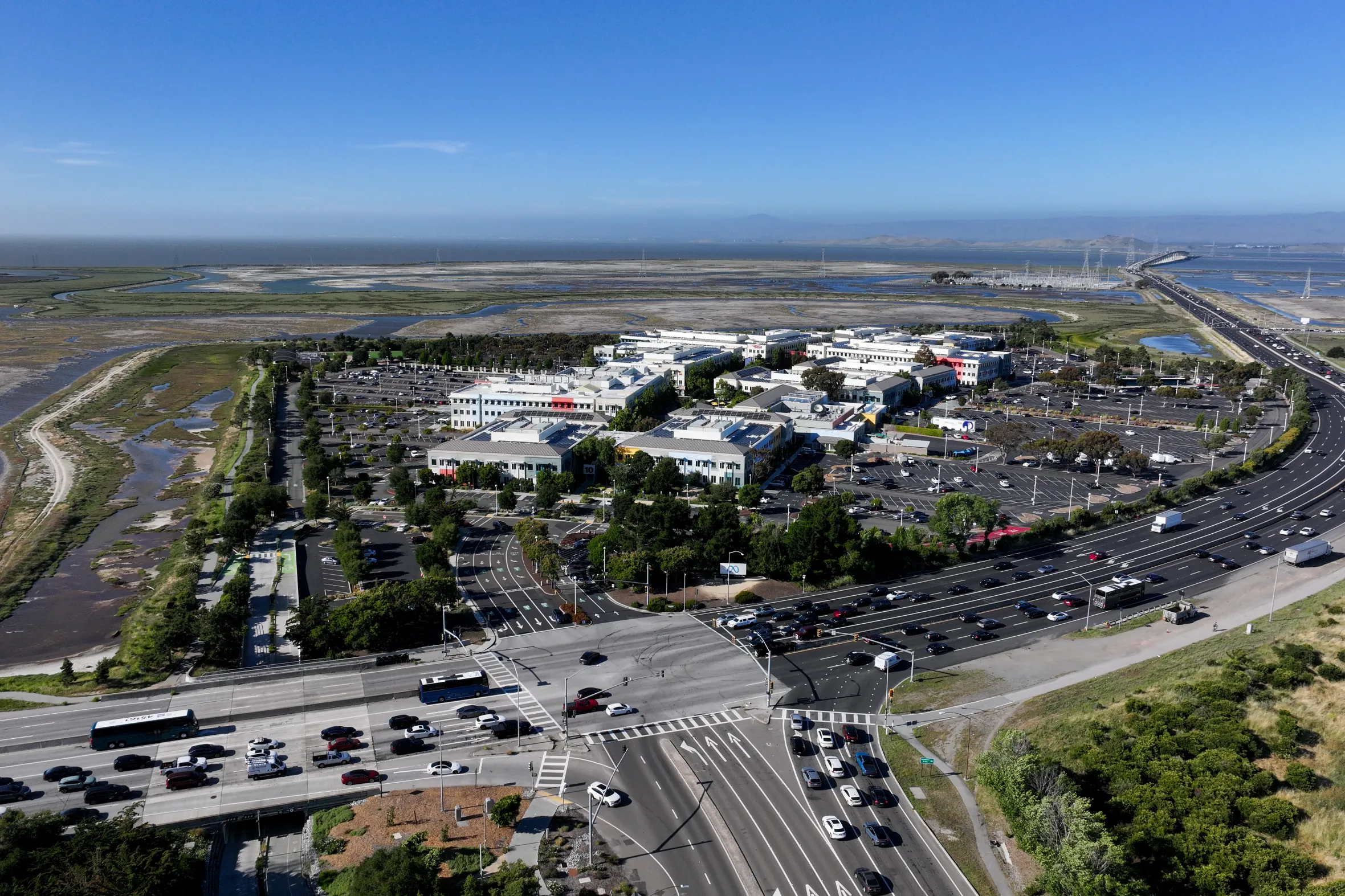 An aerial view of the Meta (Facebook) headquarters in Menlo Park, California, with the Dumbarton Bridge and San Francisco Bay in the background.