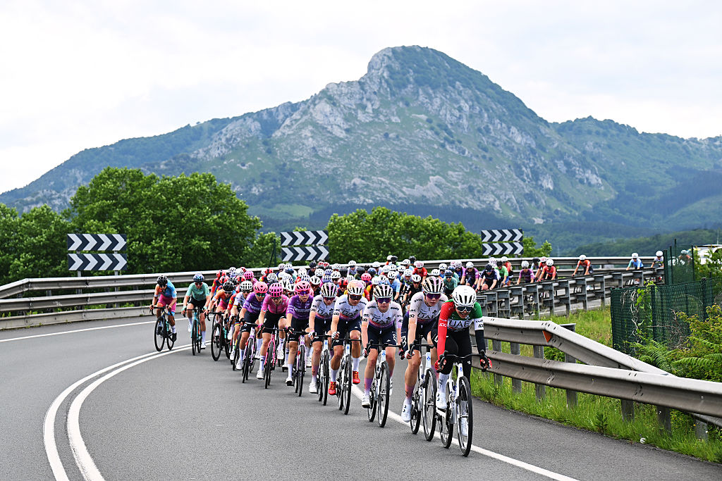 The peloton rides on a curve with mountains behind