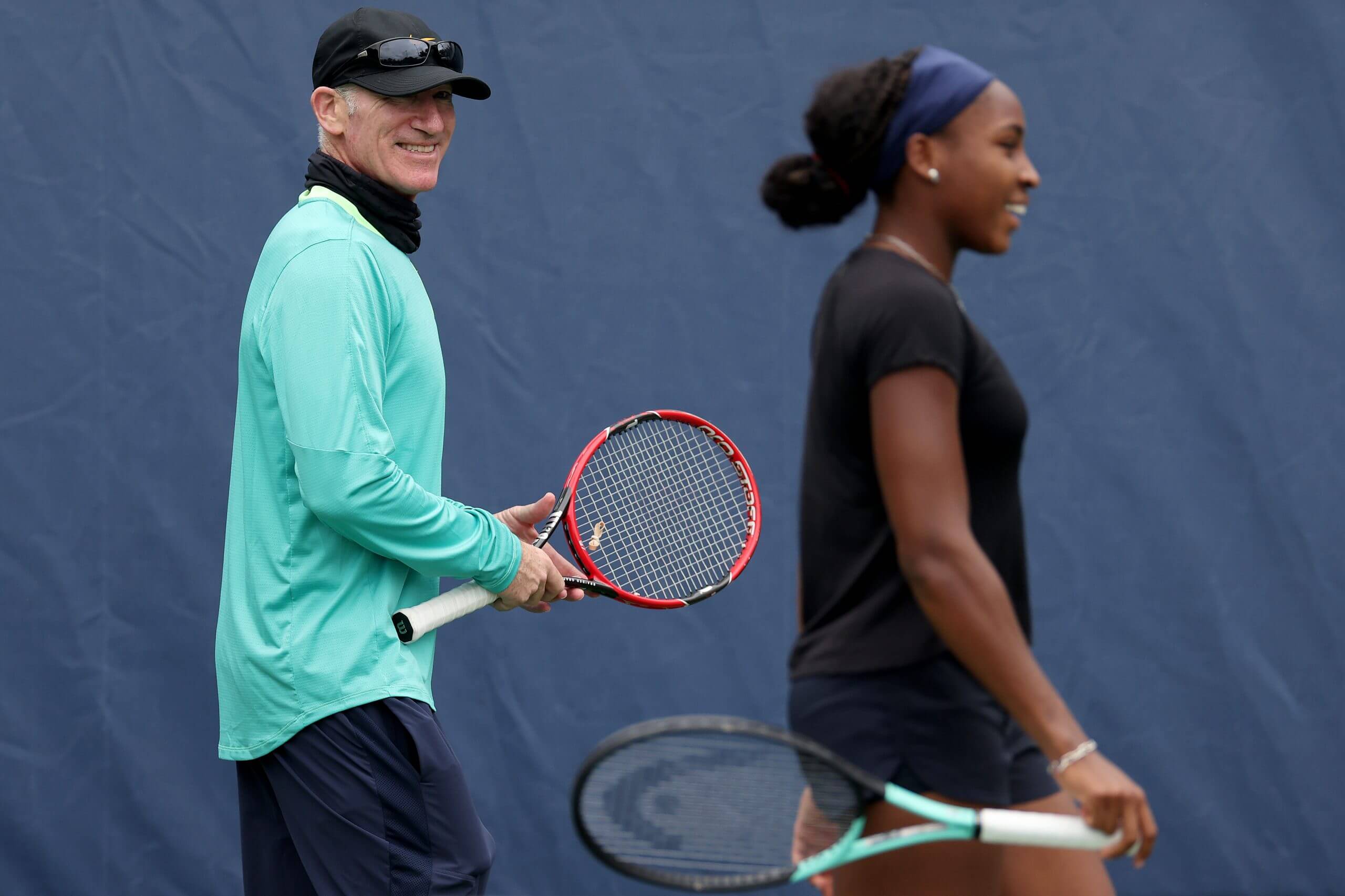Brad Gilbert and Coco Gauff smile while holding tennis rackets.