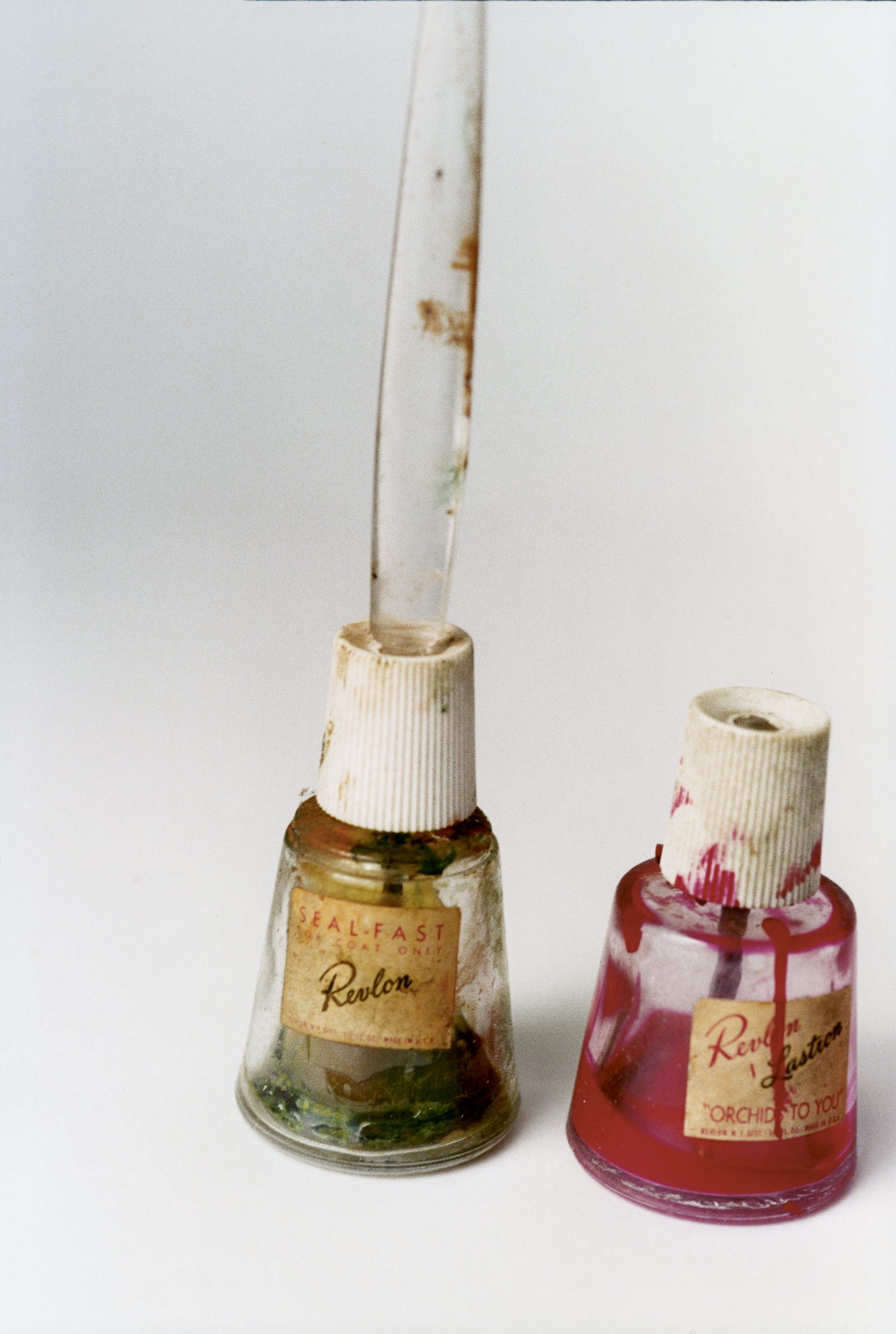 Two vintage cosmetic bottles with faded Revlon labels, showing oxidation and wear marks from age and use.