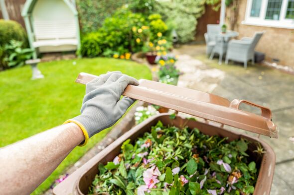 Gardener with a glove opening lid of a brown bin