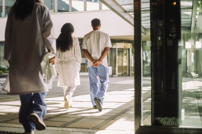 Rear view of male and female medical professionals walking together near hospital building