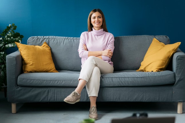 Portrait of happy young woman with arms crossed sitting on gray sofa