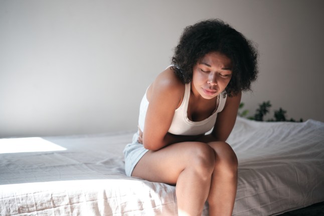 PMS symptoms. Young African American woman touching belly suffers from stomachache at home